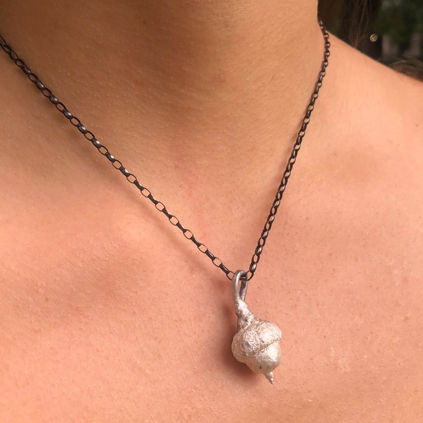 Eine Frau trägt einen filigranen Eichelanhänger aus Silber, der die Verbindung zur Natur und die innere Stärke repräsentiert.