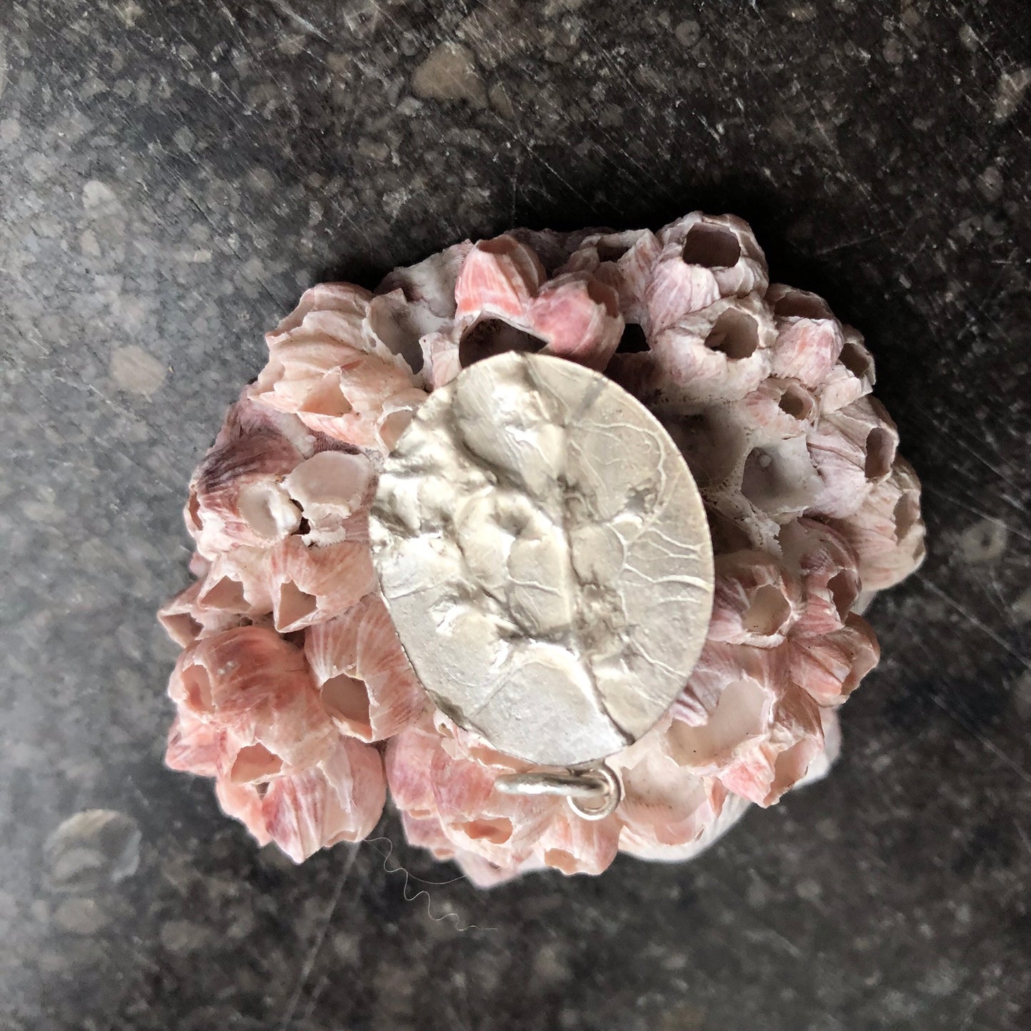 Ovaler Kettenanhänger aus Silber mit dreidimensionalen Blümchen auf einer großen Muschel liegend.