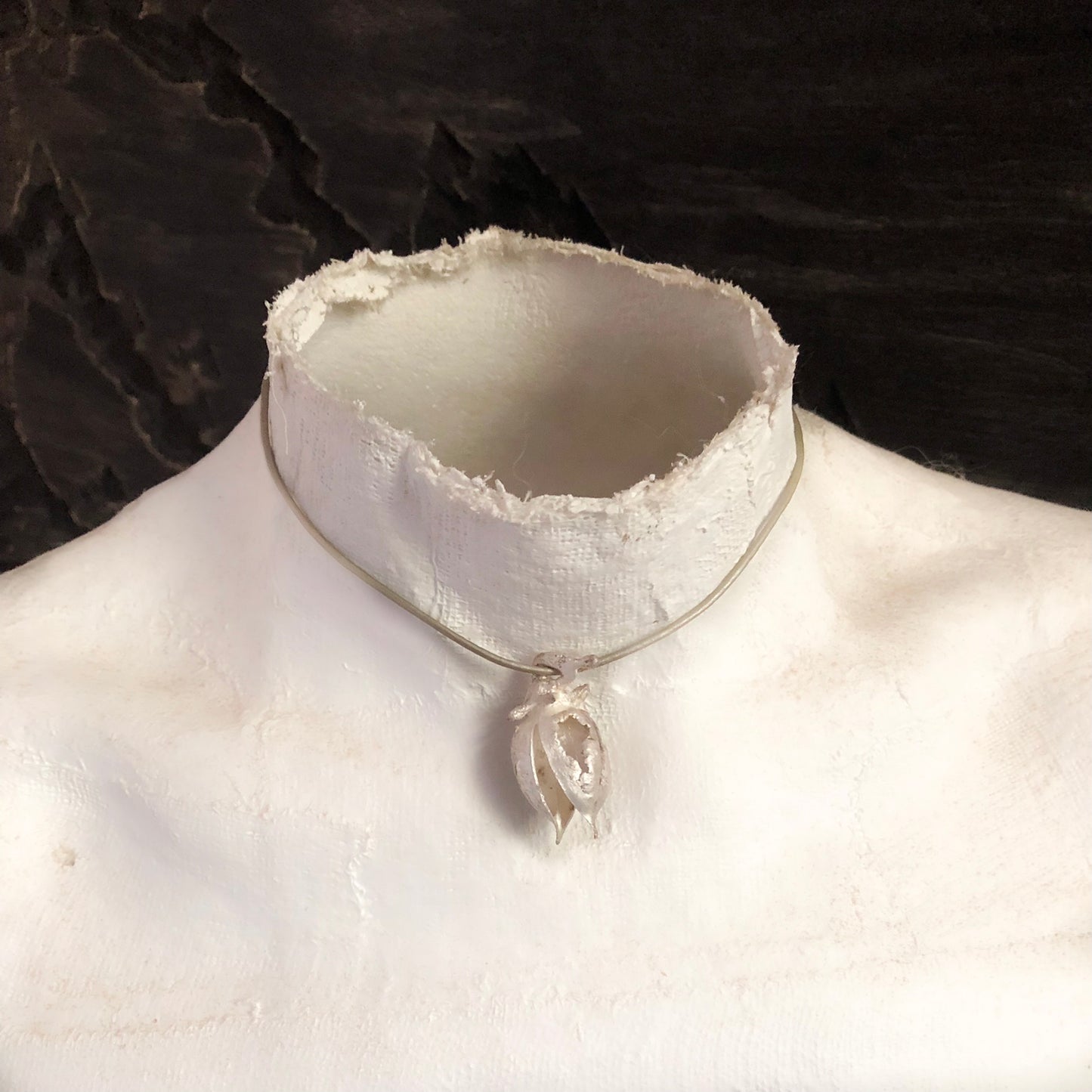 Eine Büste trägt einen silbernen Kettenanhänher in Form einer Kapsel.