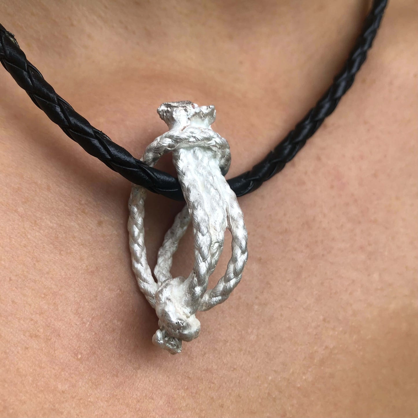 Silberner Knotenanhänger an einem Lederband getragen.