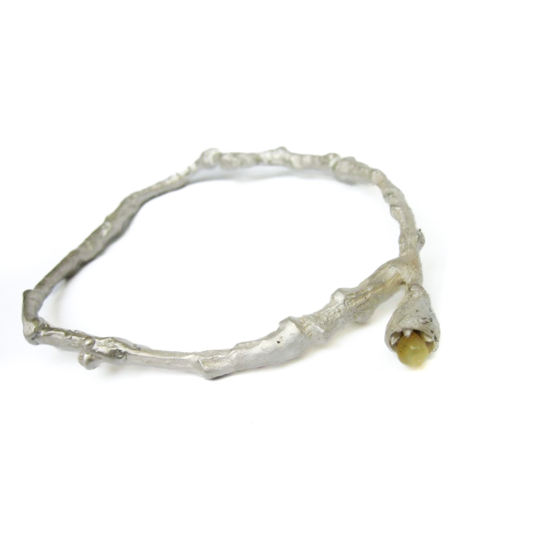 Armreif in Astform aus Silber. Von dem rechts eine Kapsel abgeht die einen Bernstein hält.