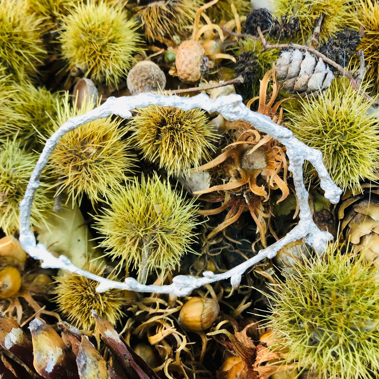 Armreif in Form eines Asts auf Kastanien und anderen Naturstücken liegend