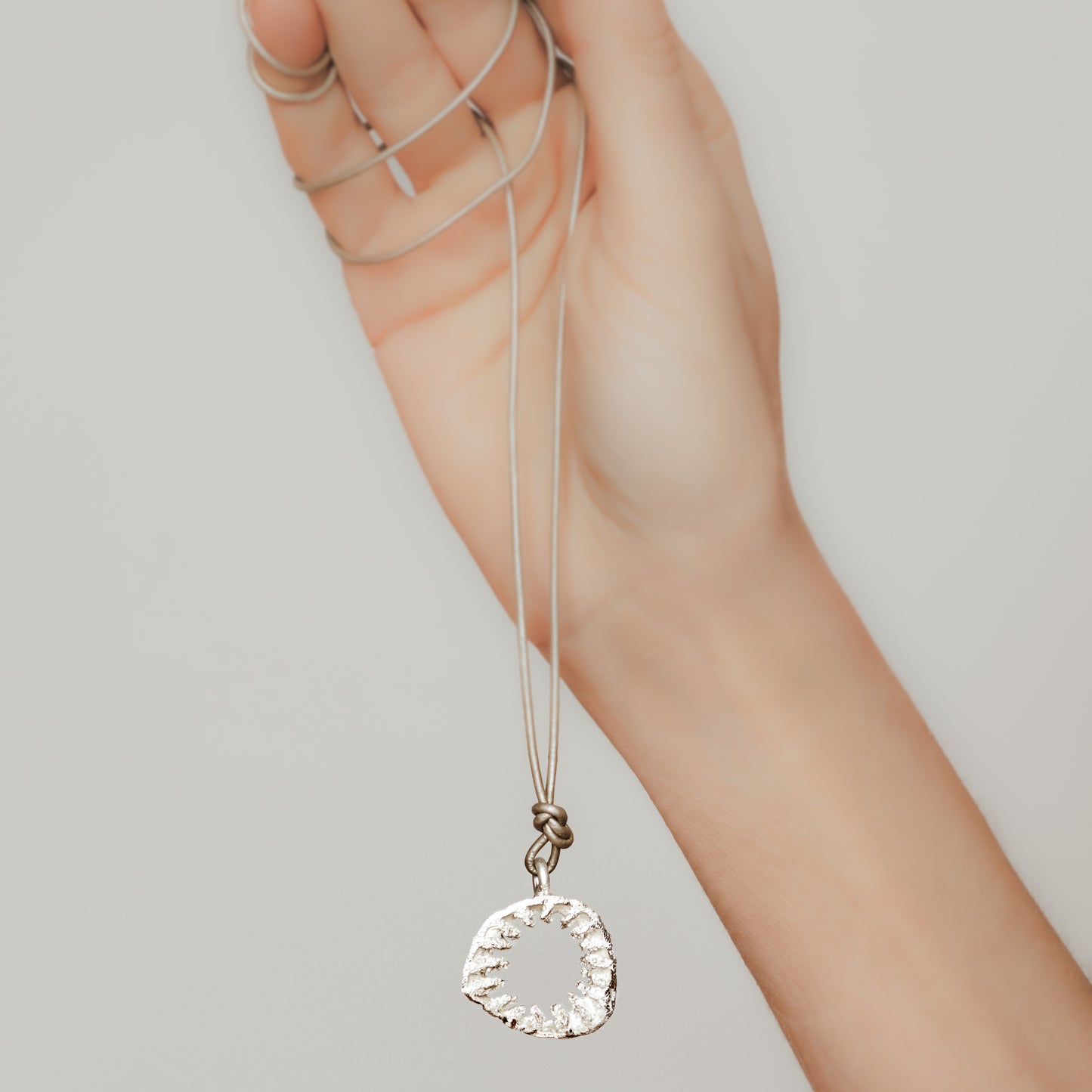 Naturinspirierter Silberanhänger der an einer silbrig-goldenen Lederschnur von einer Frauenhand gehalten wird.