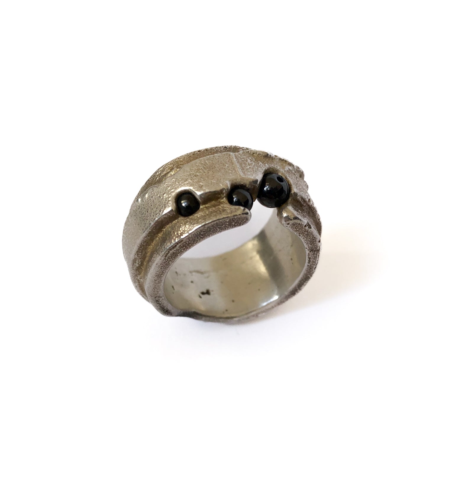 Freigestellter breiter Silberring mit drei Hämatitkugeln und sichtbarer Guss-Struktur auf weißem Hintergrund.