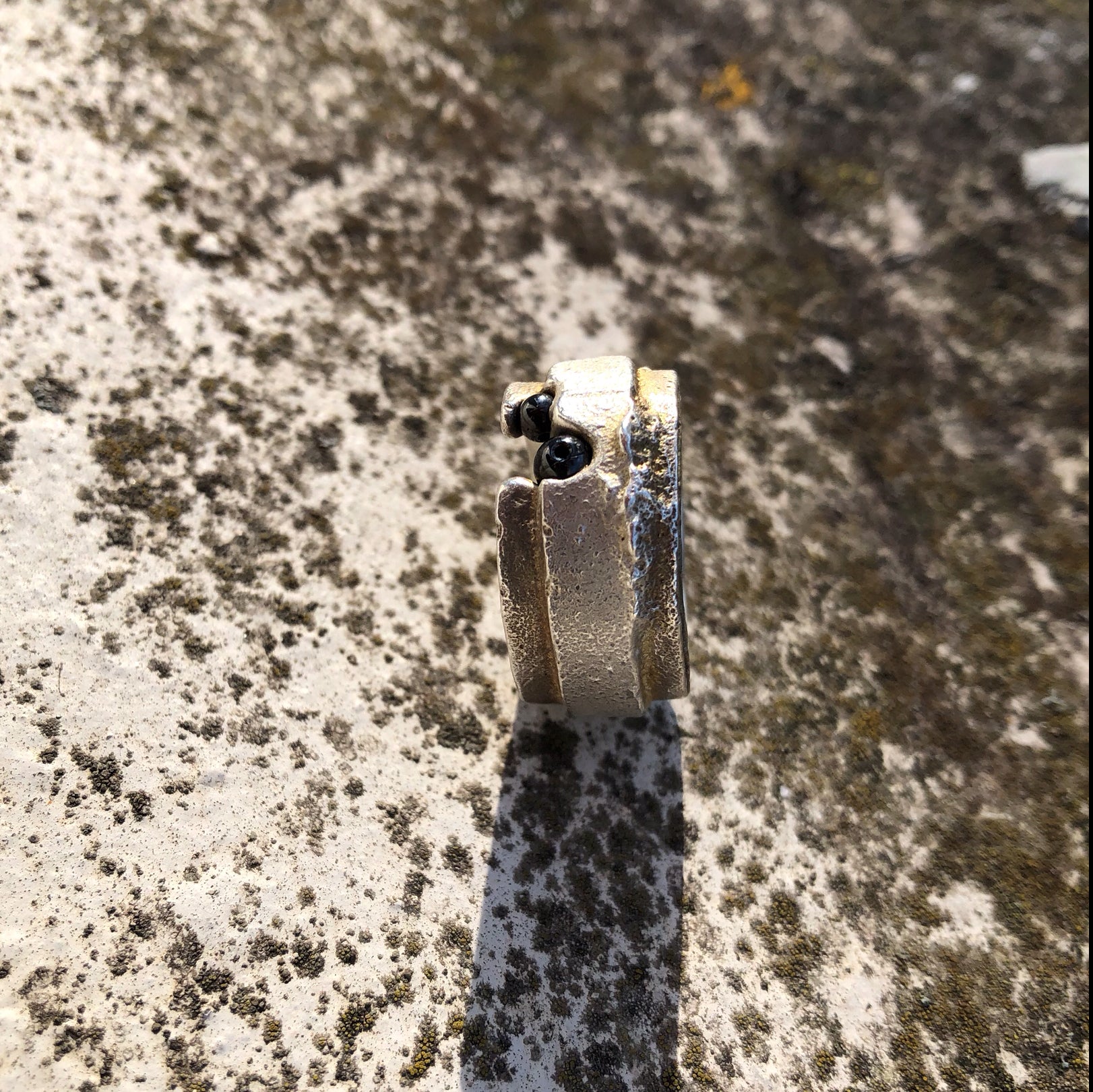 Ästhetische Schmuckpräsentation eines massiven Silberunikat-Rings mit Hämatit in einer Moos-Landschaft.