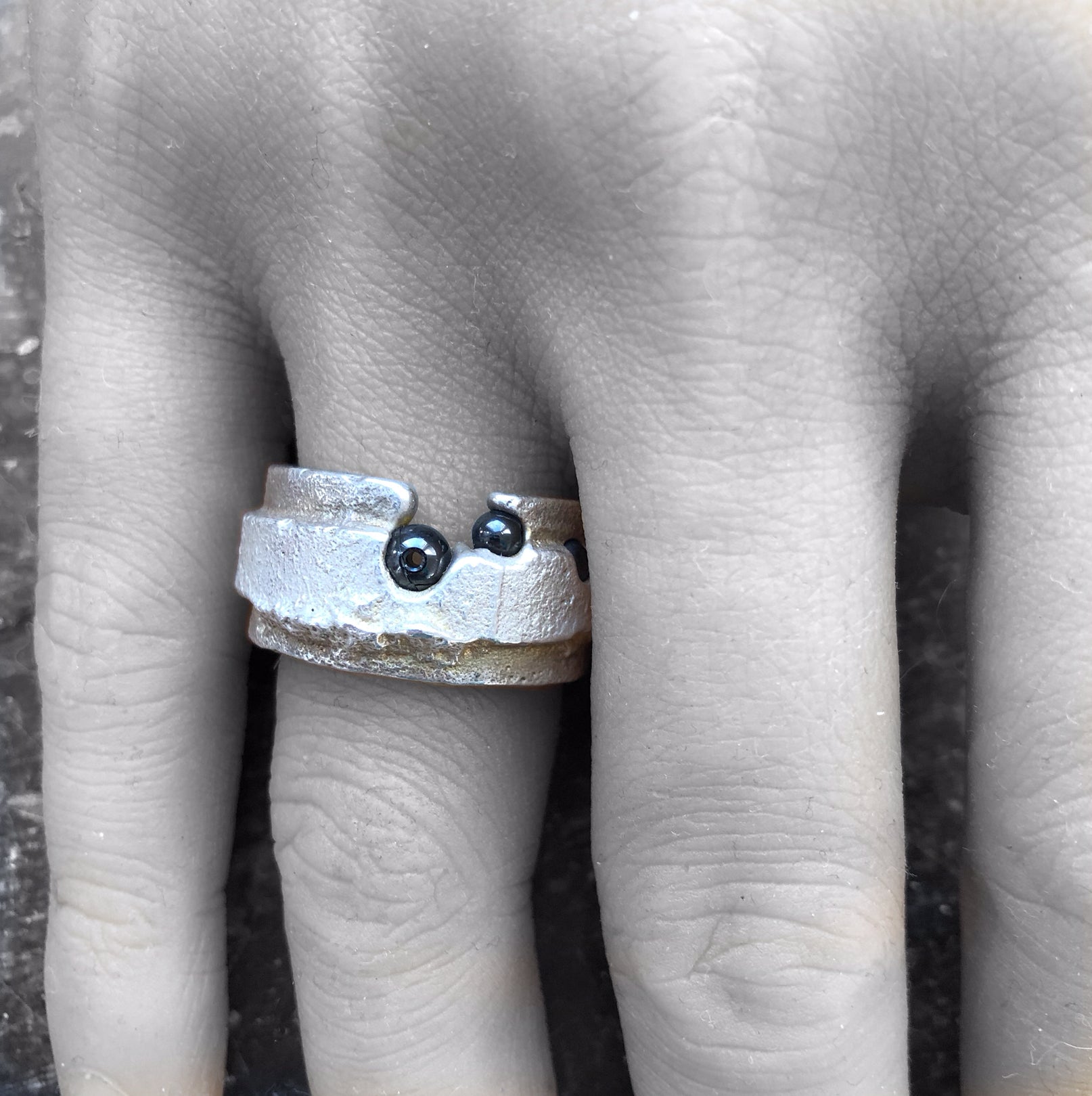 Massiver Silberring an einer Hand vor schwarz-weißem Hintergrund, das Silber und die Hämatite in natürlichen Farben.