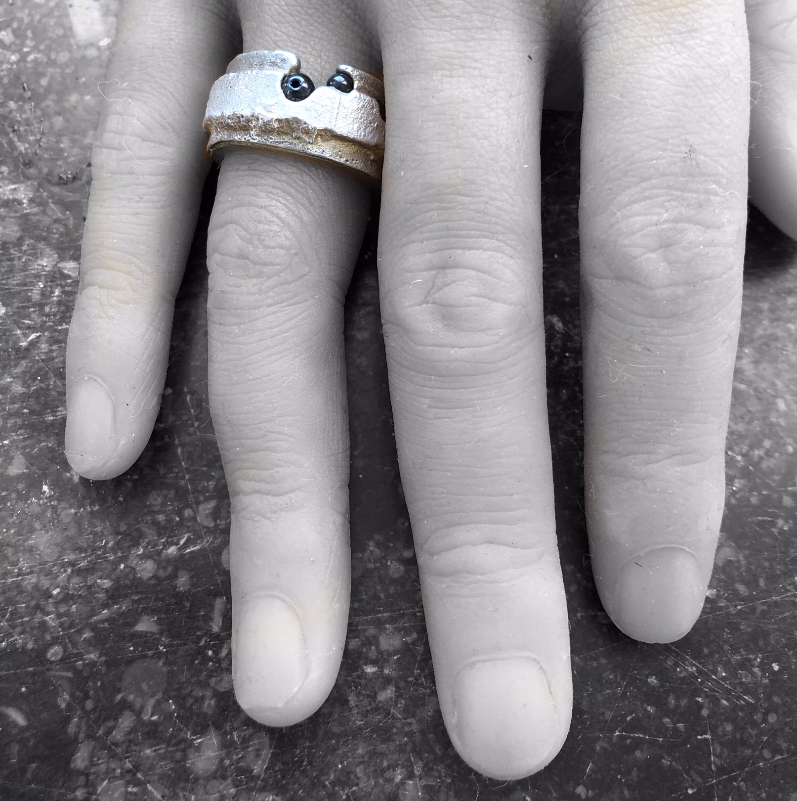 Der massive Ring am Finger, die goldigen Seiten und das Silber leuchten farbig vor einem monochromen Hintergrund.