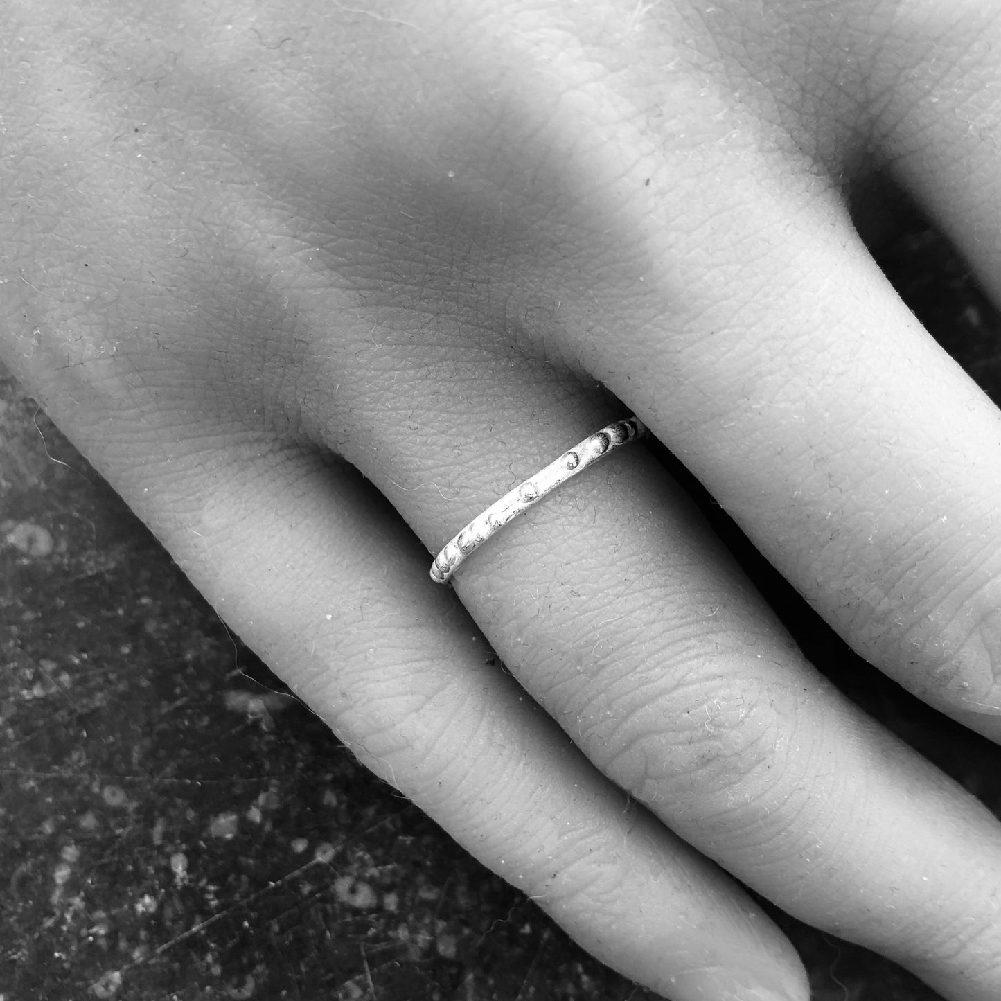 Künstlerische Schwarz-Weiß-Aufnahme eines zarten Kügelchen-Rings am Finger, der die feine Textur und das Spiel von Licht und Schatten betont.
